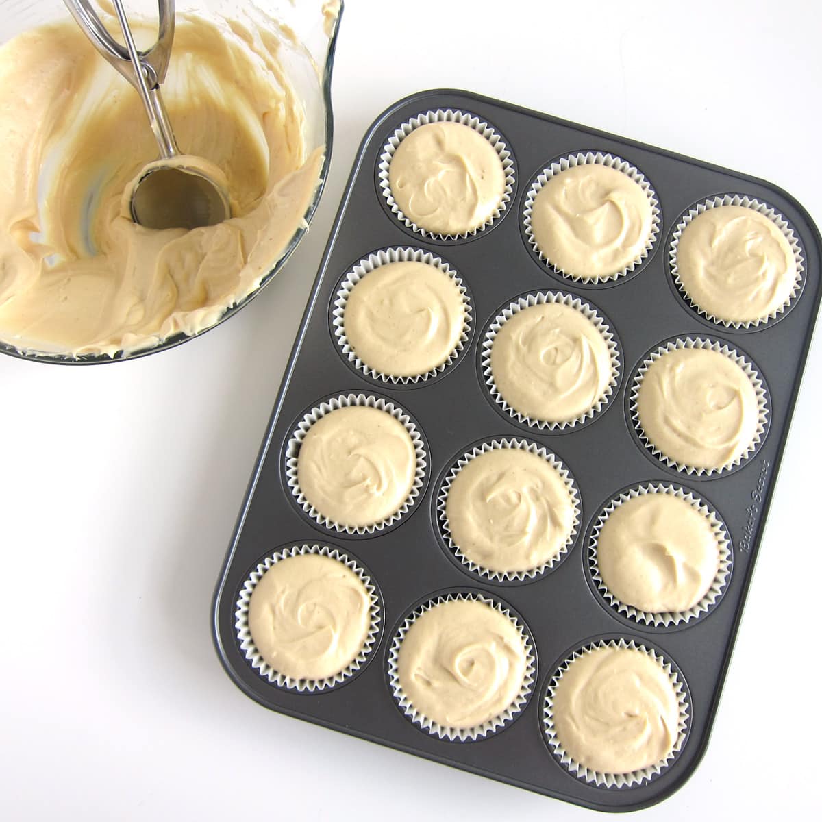 Peanut butter cheesecake filling spooned into cupcake wrappers in a muffin tin.
