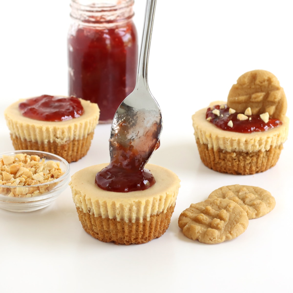 Pouring jelly over a minipeanut butter cheesecake that is next to peanut butter cookies, and pb&j cheesecakes.