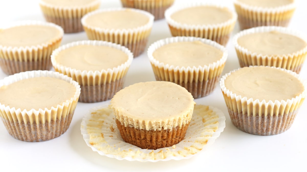 Mini peanut butter cheesecakes in paper cupcake wrappers. One is unwrapped.