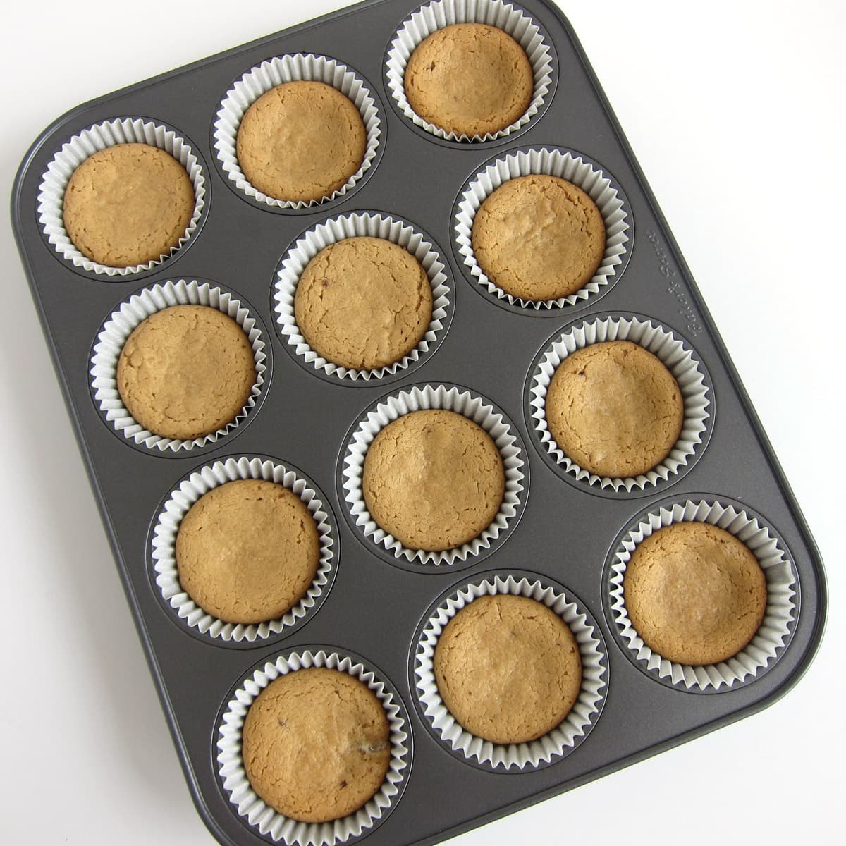 Baked peanut butter cookie cups in cupcake wrappers in a muffin tin.