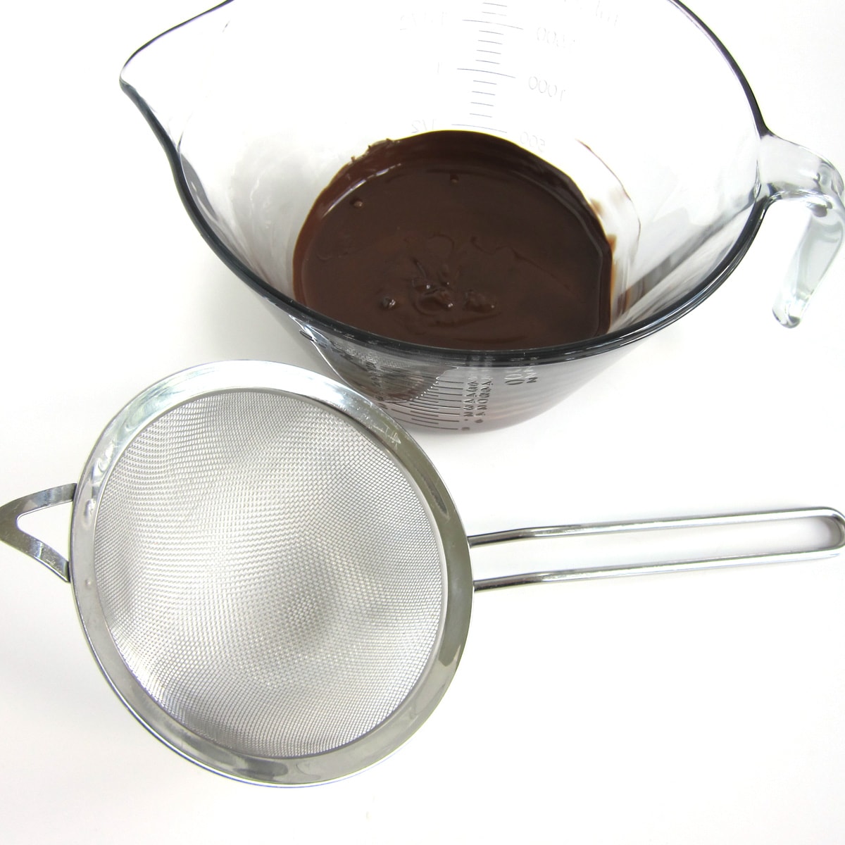 melted chocolate in a mixing bowl set next to a fine mesh sieve