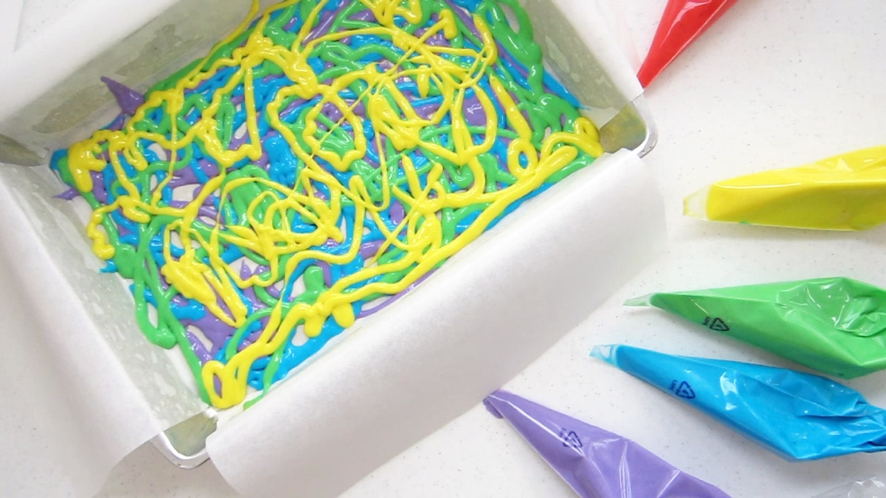 yellow cake batter swirled over layers of green, blue, and purple cake batter.