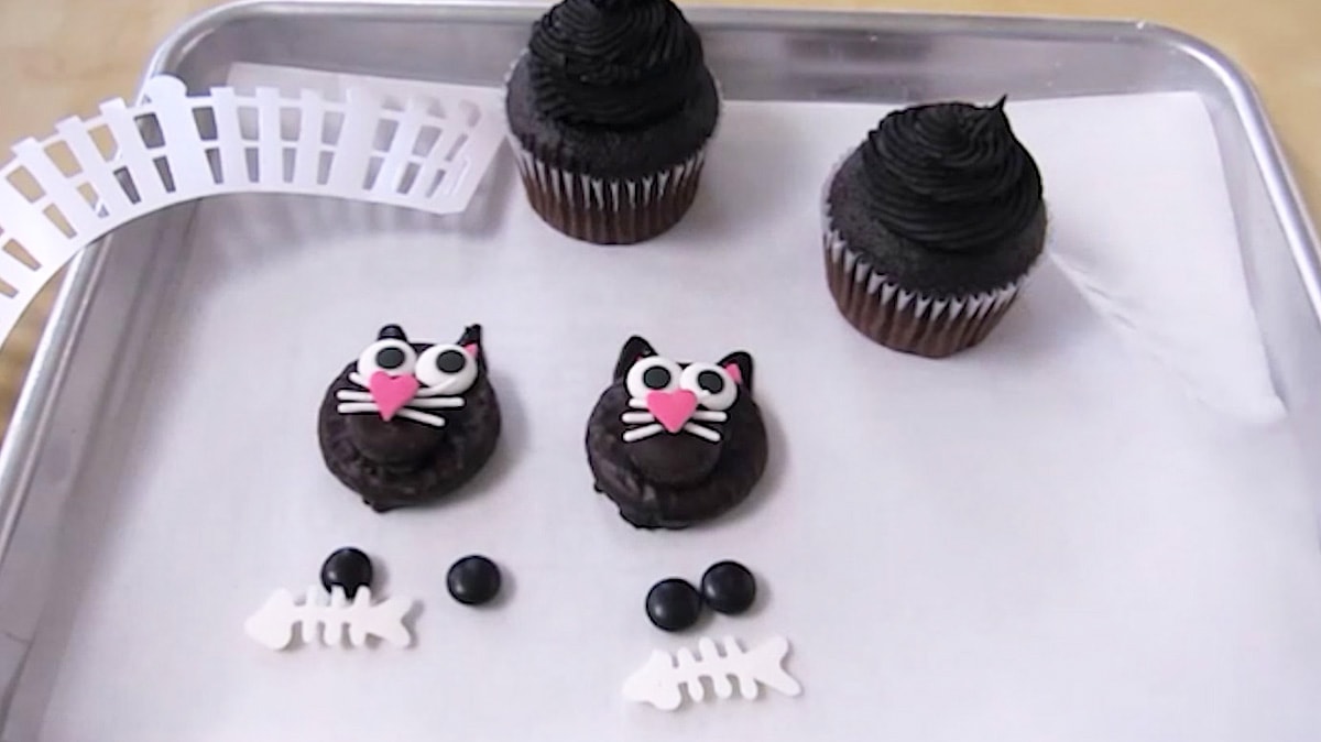 Peppermint Patty black cats with two black M&Ms, white chocolate fish bones, chocolate cupcakes, and a white picket fence cupcake wrapper.