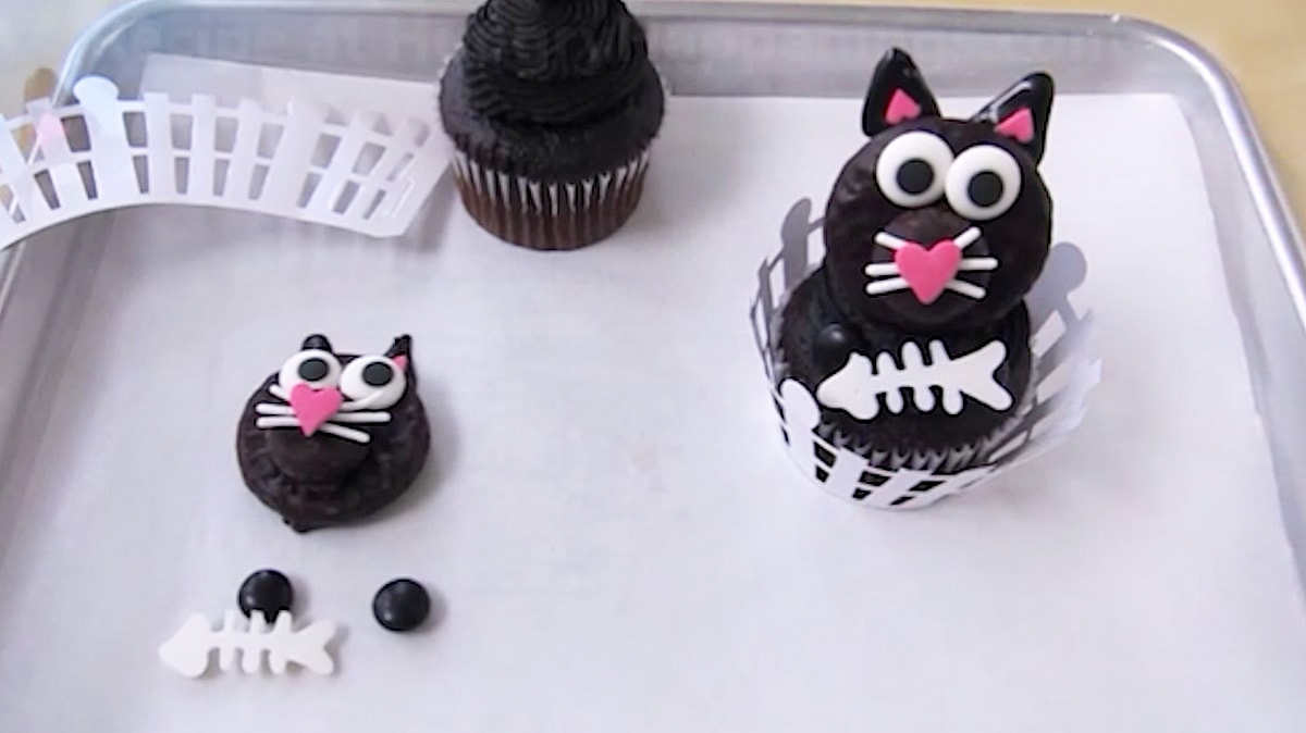 assembled black cat cupcake with a Peppermint Patty head decorated with candy and sprinkles, white chocolate fish bones, and two black M&M paws.
