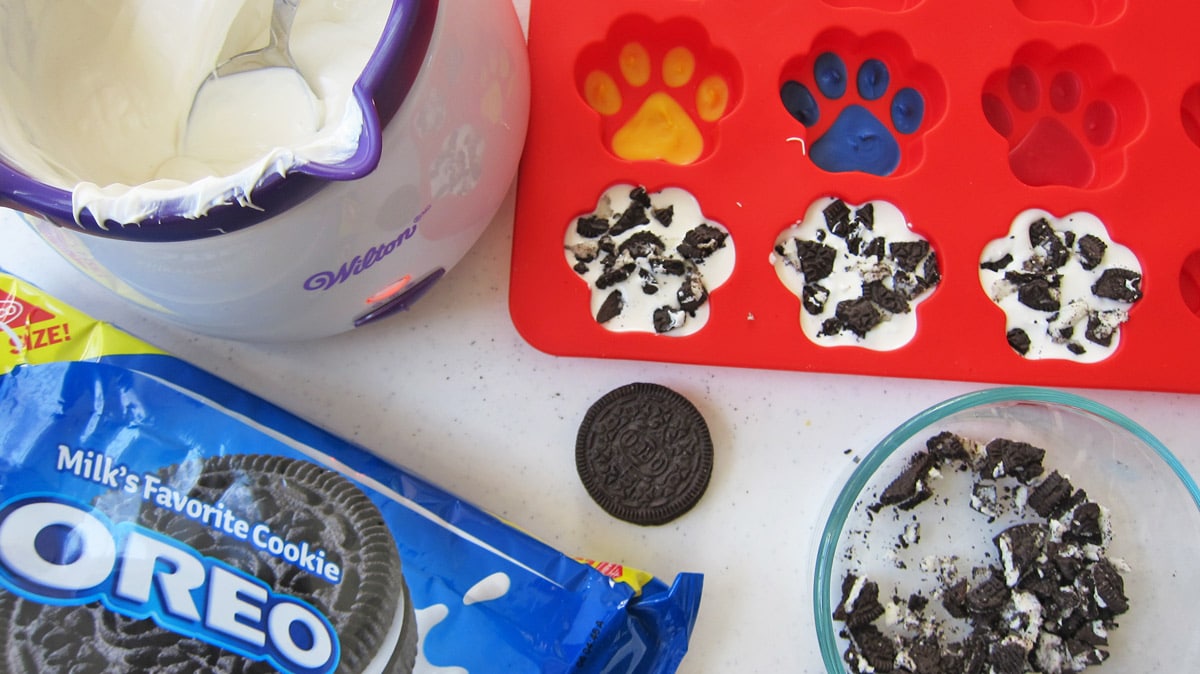 white chocolate in a Wilton melter, silicone paw mold painted and filled with white chocolate and OREO Cookie pieces, and OREOs.