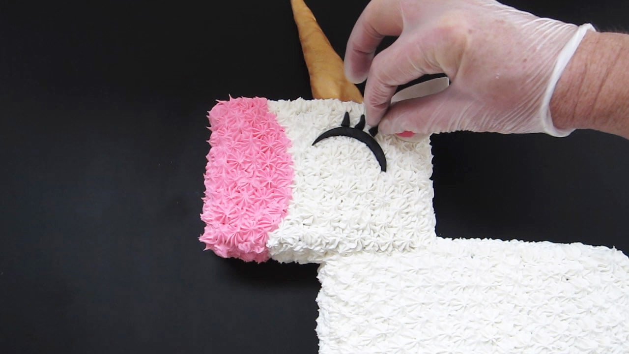 adding black modeling chocolate eyelashes to the unicorn cake.
