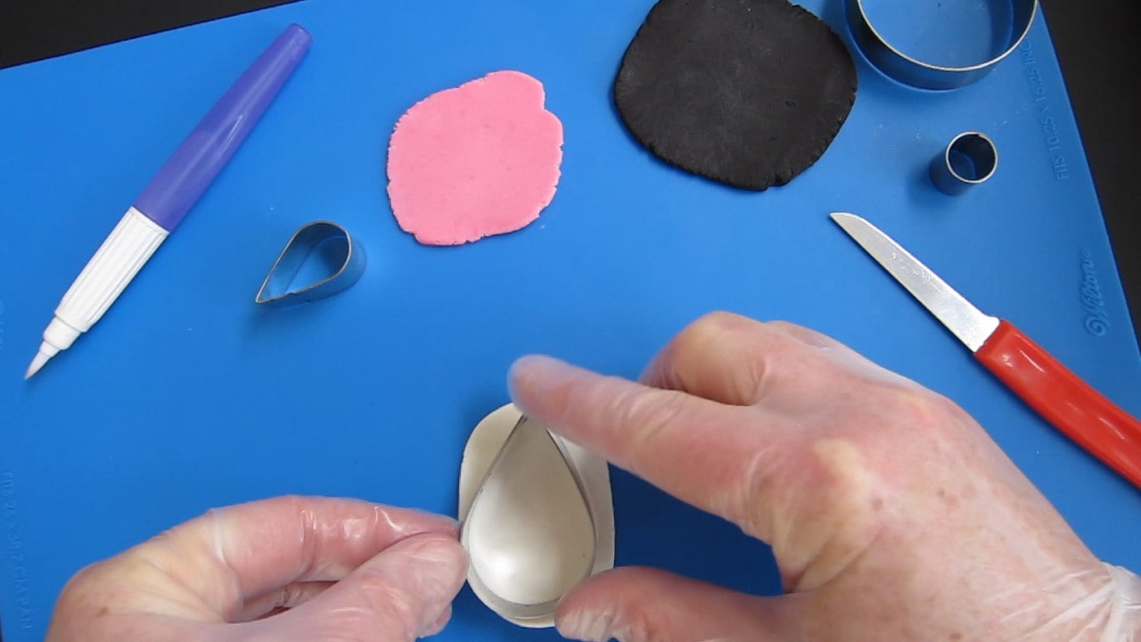 cutting white modeling chocolate using a large teardrop cookie cutter.
