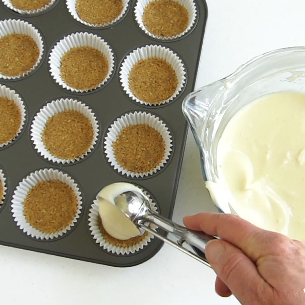 Spoon cheesecake filling over mini graham cracker crusts in cupcake pan.