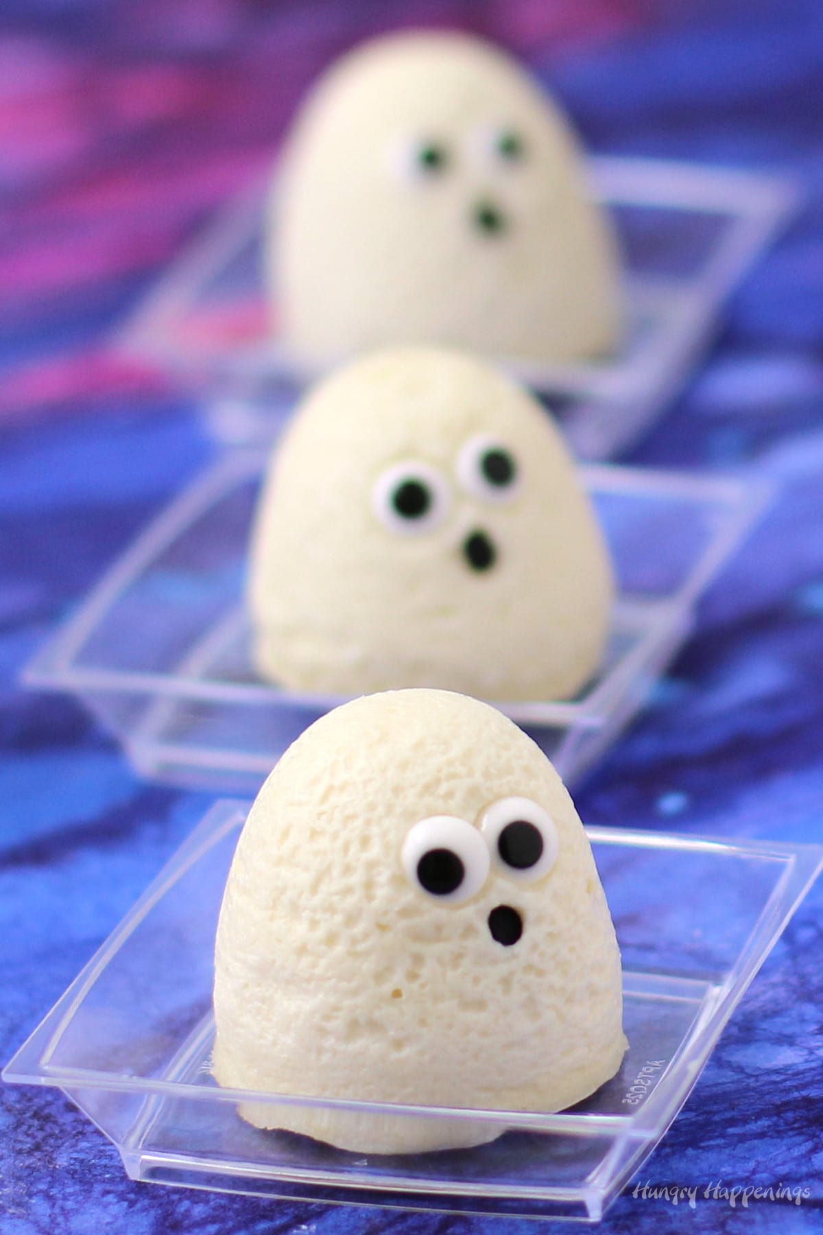 little Halloween cheesecake ghosts with candy eyes and black confetti sprinkle mouths.