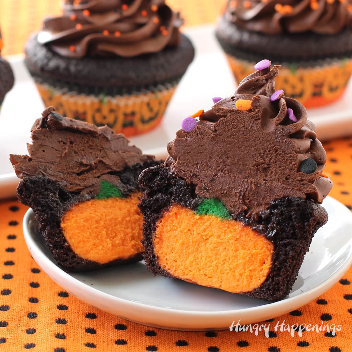 chocolate Halloween cupcakes stuffed with cheesecake pumpkins are frosted with chocolate ganache frosting with Halloween sprinkles on top