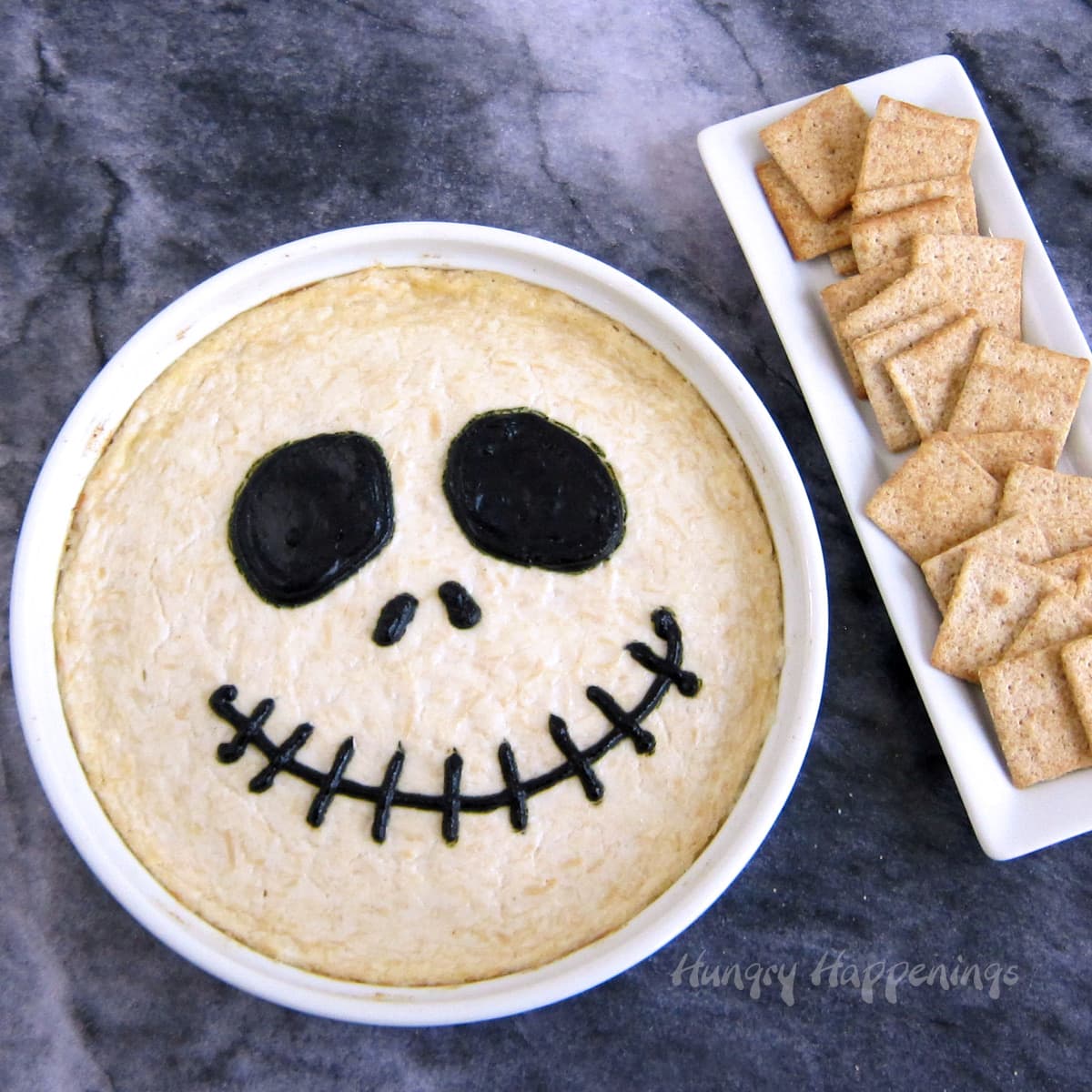 Jack Skellington Dip - a chicken dip decorated with black-colored cream cheese to look like this Nightmare Before Christmas character is served next to crackers.