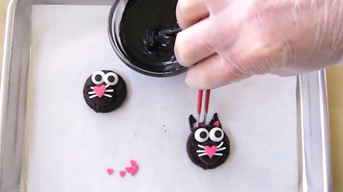adding pink heart-shaped sprinkles to the black cat's ears.