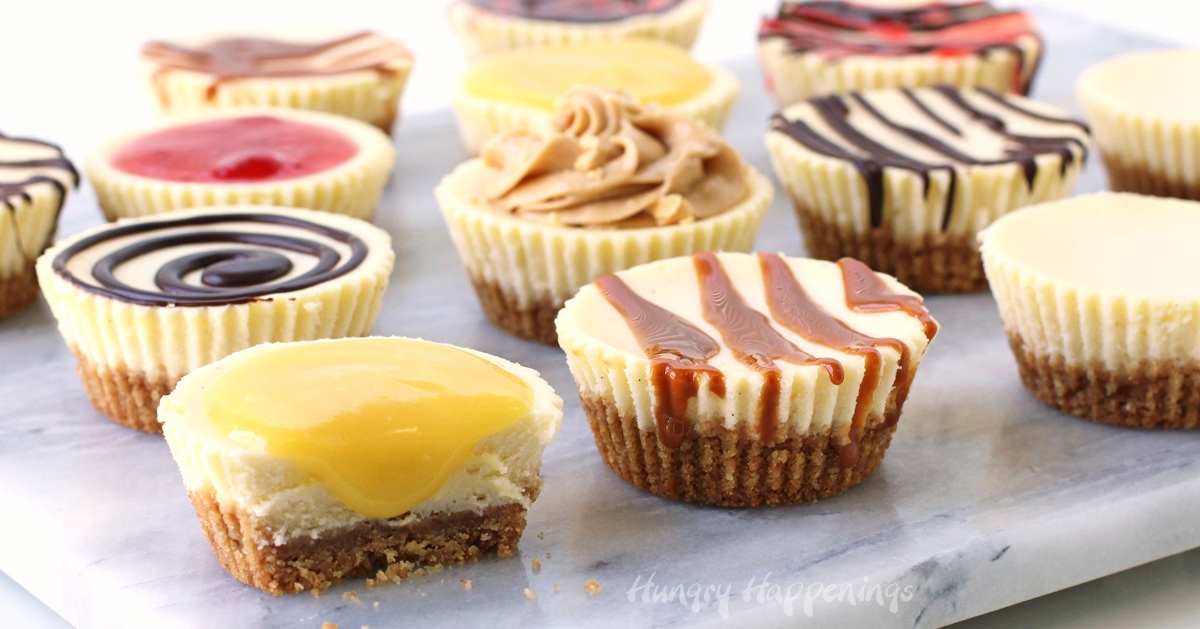 Mini baked cheesecakes topped with lemon curd, caramel sauce, chocolate ganache, peanut butter mousse, and strawberry sauce. 