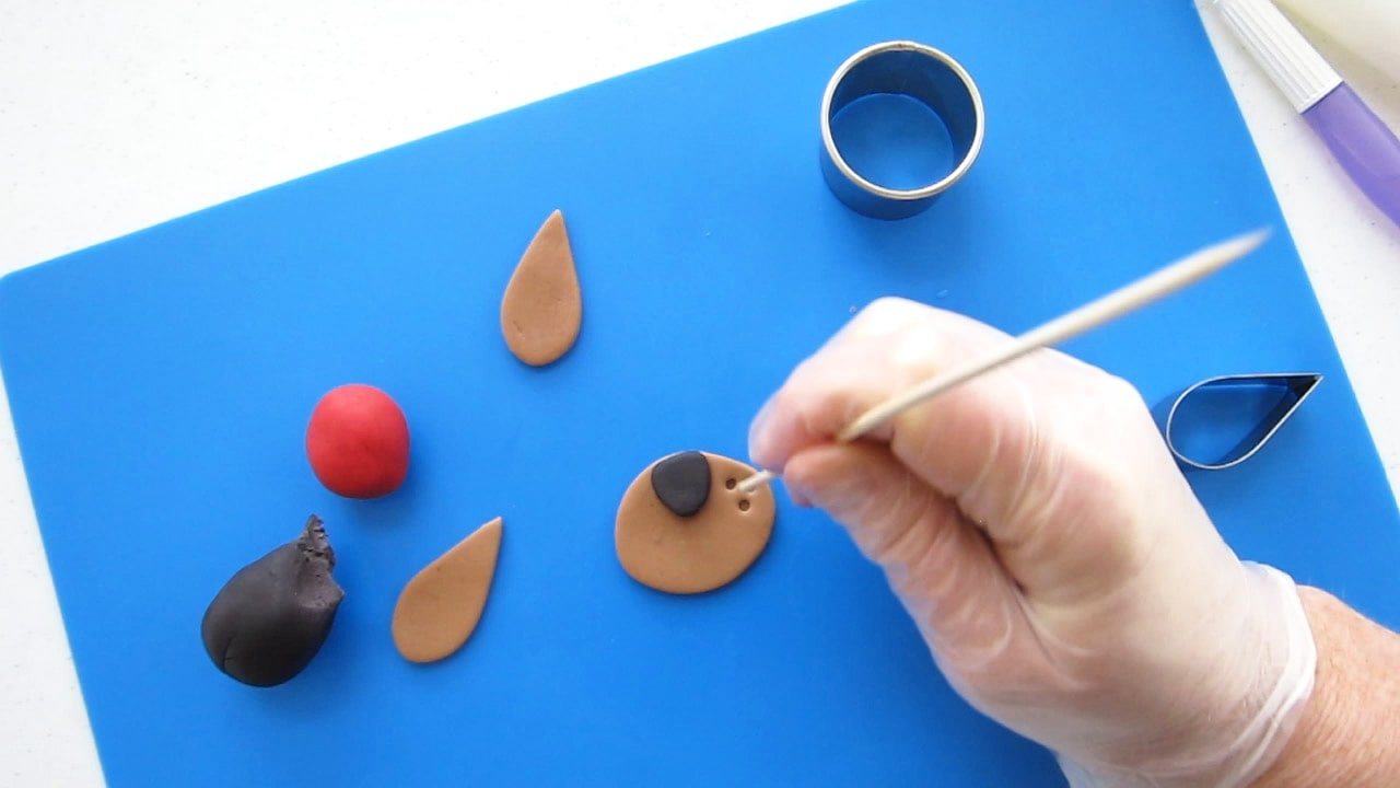 making dimples in a modeling chocolate dog snout using a wooden skewer.
