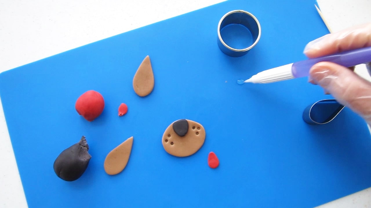 modeling chocolate dog nose, ear, and tongue, on a blue silicone mat with a water pen and cookie cutters.