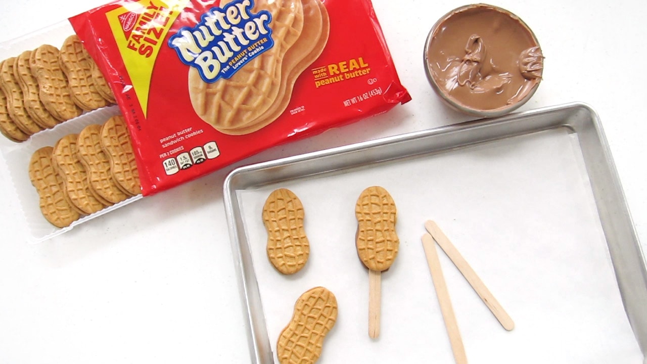 a package of Nutter butter Cookies, a bowl of melted chocolate, and a tray of Nutter Butter Cookies and pops.