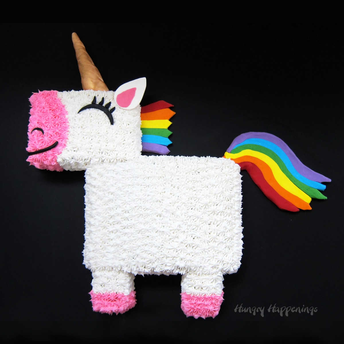 white and pink unicorn cake with a rainbow mane and tail, gold horn, and black eyelashes.