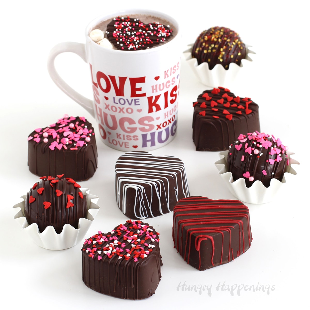 Valentine's Day hot chocolate bombs hearts and spheres alongside a Valentine's Day mug filled with hot chocolate.