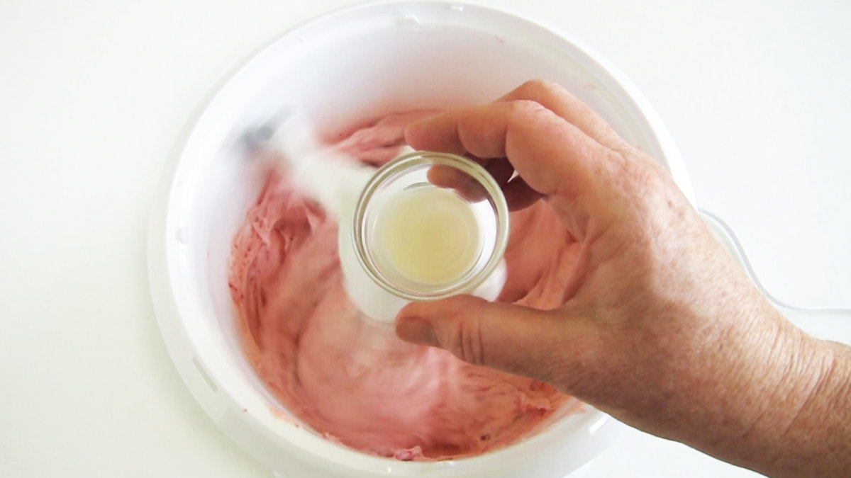 adding lemon juice to the strawberry frosting in the mixing bowl.