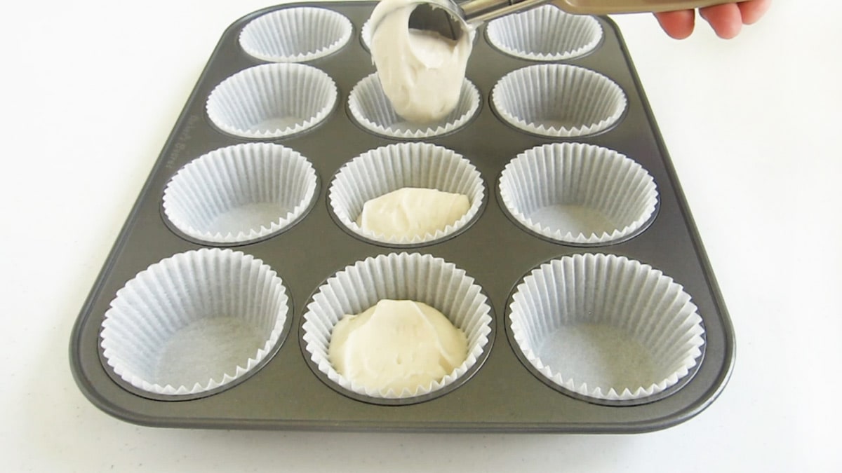 scooping white cake mix into cupcake wrappers in a non-stick cupcake pan.
