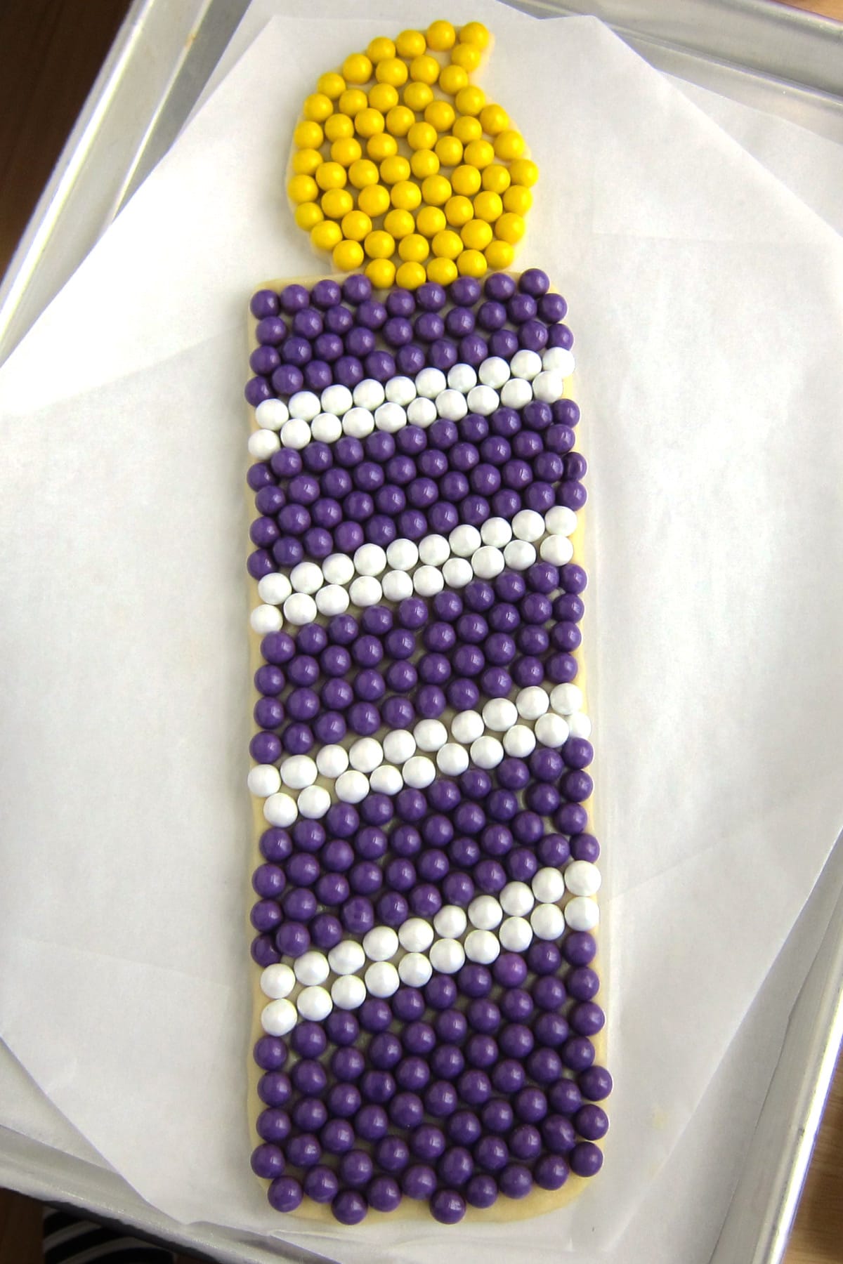 birthday candle cookie decorated with stripes of purple and white Sixlets candies and yellow candies on the flame.