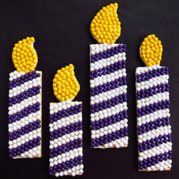 birthday candle cookies decorated with blue and white stripes and a yellow flame made from Sixlets chocolate candies.