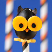 closeup of one black olive owl with big yellow cheese eyes, an orange carrot beak, and orange cheese feet.