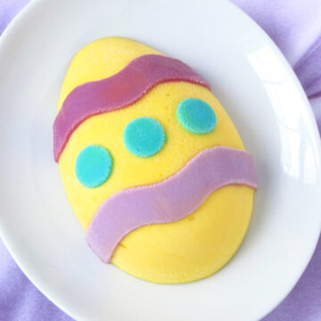 a yellow hand-painted cheesecake Easter egg with purple wavy stripes and turquoise polka dots served on a white dish on a piece of lavender satin.