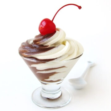 chocolate cheesecake mousse with swirls of chocolate mousse and cheesecake mousse topped with a maraschino cherry in a glass dessert cup with a white spoon