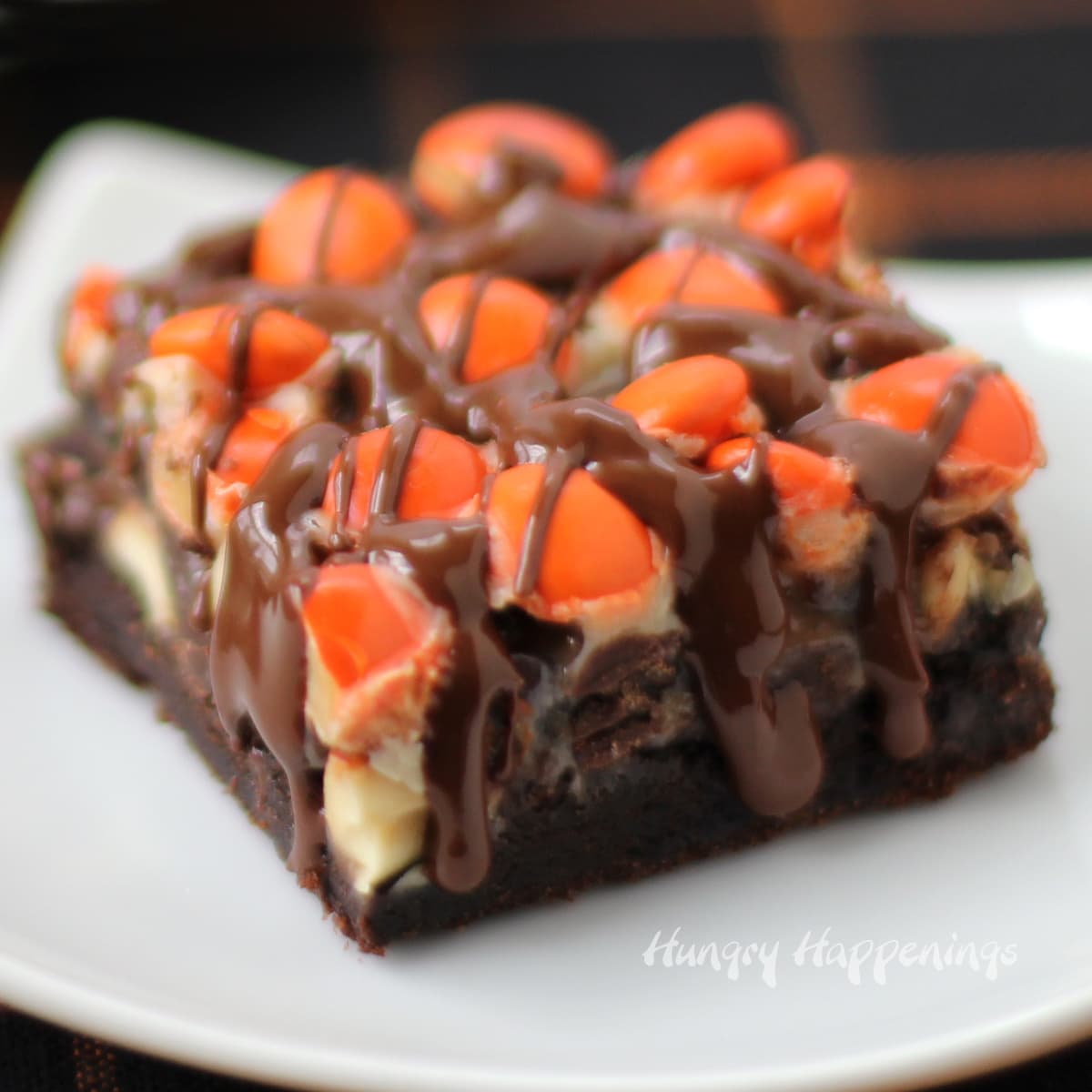 one chocolate magic bar topped with peanuts, Reese's Pieces, and chocolate glaze served on a small white plate.