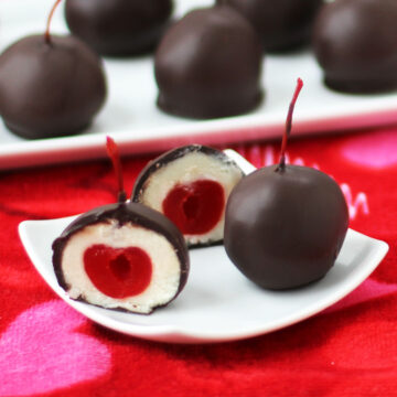chocolate cordial cherry cake balls filled with white cake ball dough and a maraschino cherry on white plates on a Valentine's Day towel.