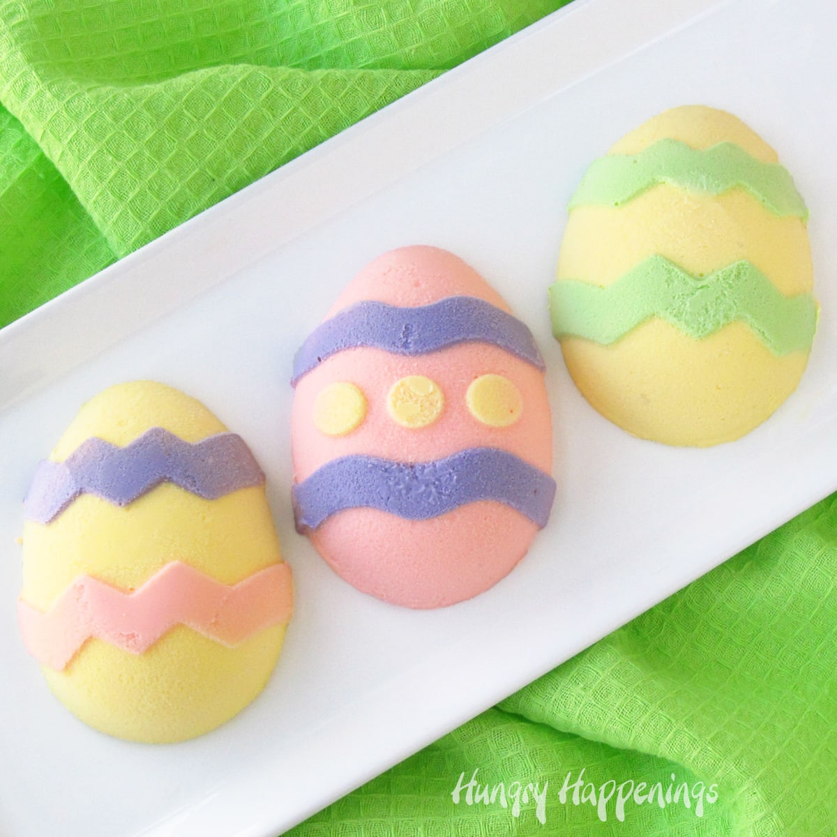 yellow and pink pastel-colored hand-painted cheesecake Easter eggs on a white plate on a green napkin.