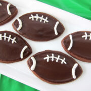 chocolate football cookies decorated with chocolate and vanilla frosting served on a white platter on a green tablecloth.
