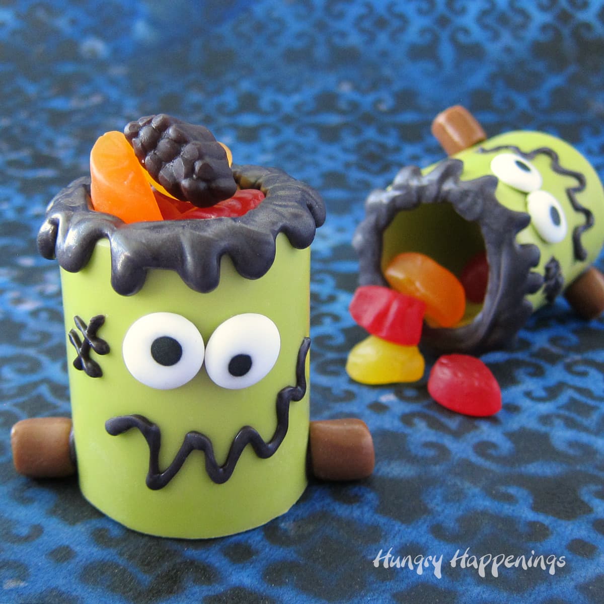 Frankenstein candy cups made out of green candy melts and decorated with candy eyes and Tootsie Roll bolts are filled with fruit snacks.