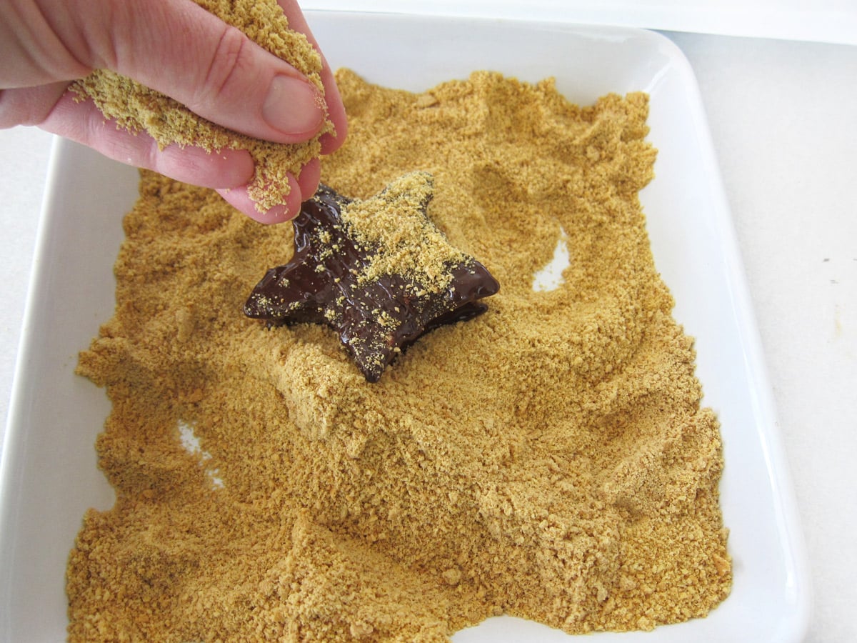 sprinkling graham cracker crumbs over a chocolate-dipped marshmallow star.