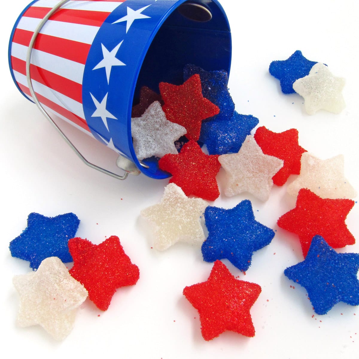 red, white, and blue gumdrop stars spilling out of a 4th of July pail onto a white table.