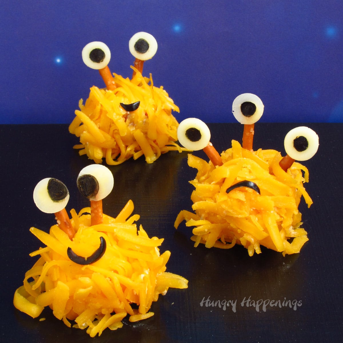 Halloween cheese ball monsters with pretzel and cheese eyes and black olive smiles.