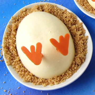 hatching chick cheesecake served on graham cracker crumbs on a white egg-shaped plate.