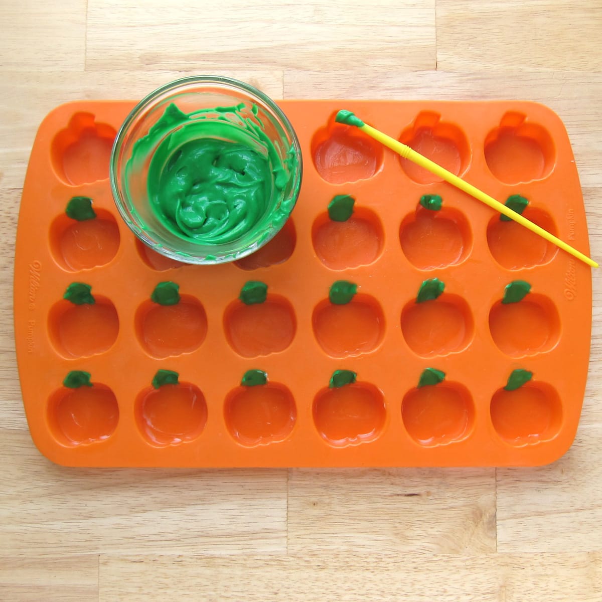 painting green cheesecake filling into the stem of the pumpkins in a silicone mold.