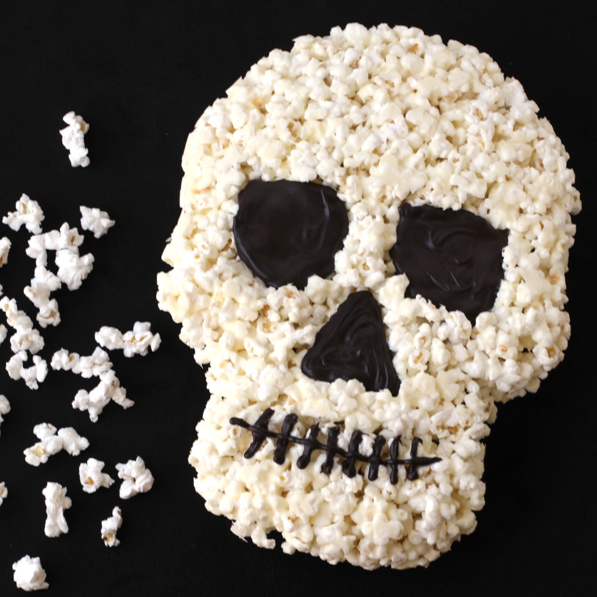 white chocolate popcorn skull on a black background with loose popcorn on the table.