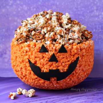 Orange pumpkin popcorn bowl filled with white chocolate popcorn drizzled with orange and black candy melts.