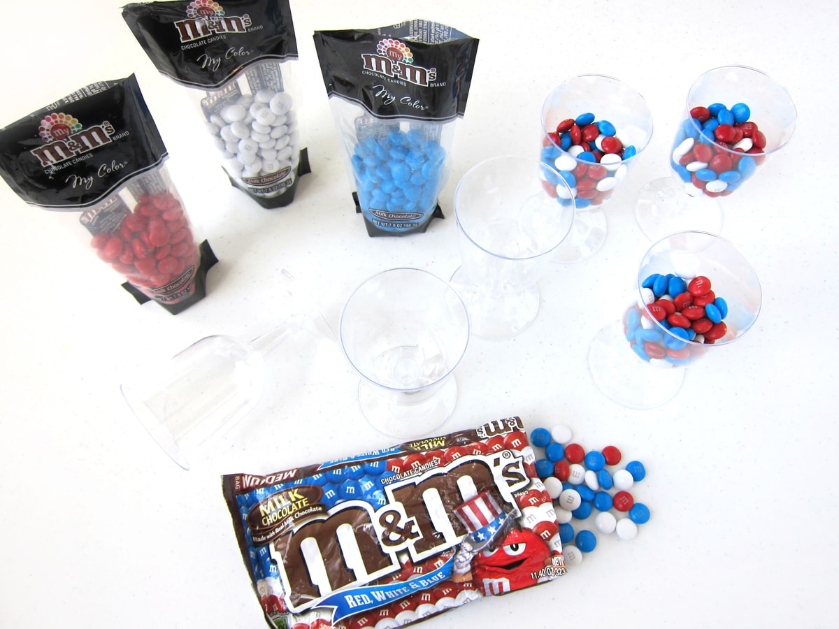 Red, white, and blue M&M's in bags an in plastic wine glasses.