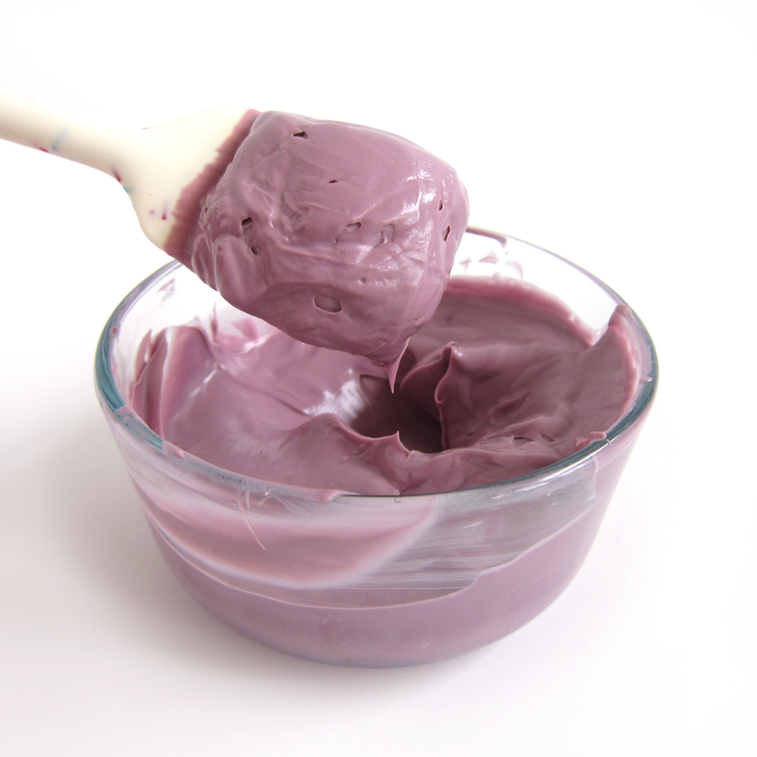 a spatula with thick candy melts above a bowl of melted purple candy melts.