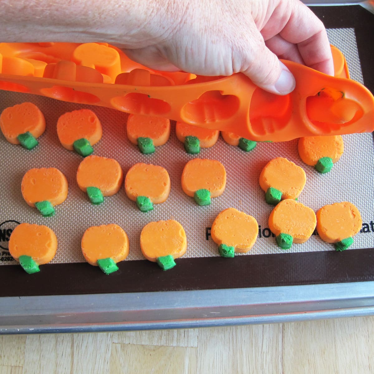 unmolding orange and green pumpkin cheesecakes from a silicone mold onto a silicone mat on a baking sheet.