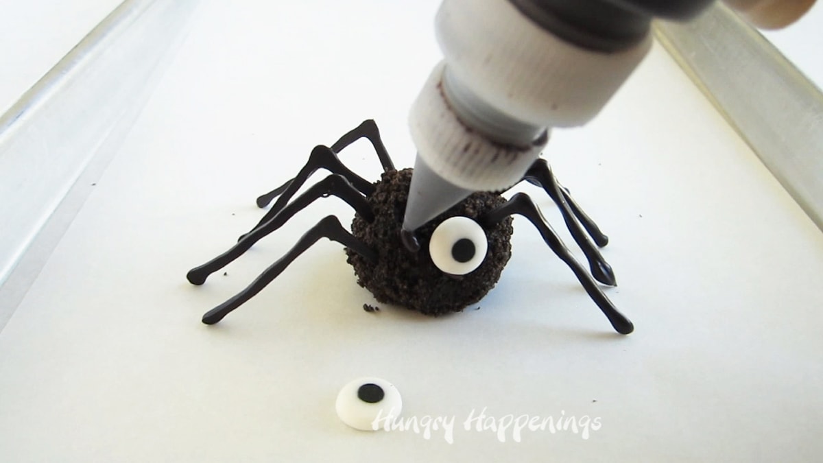 piping black candy melts onto an oreo spider to attach a candy eye.