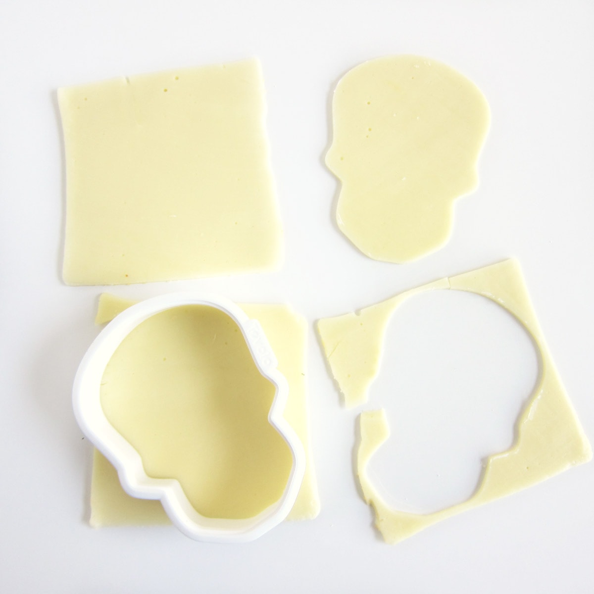 cutting white cheese slices using a skull-shaped cookie cutter. 