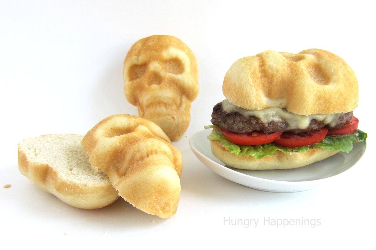 a cheeseburger served on a skull-shaped hamburger bun next to more skull-shaped homemade hamburger buns.