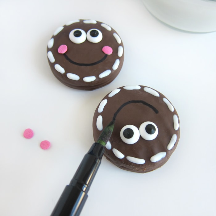 drawing a smile onto a milk chocolate OREO gingerbread man.