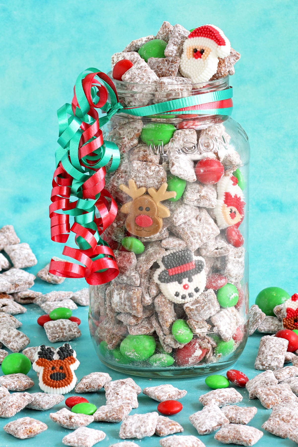 Christmas Puppy Chow packaged in a large mason jar tied with red and green curling ribbon.