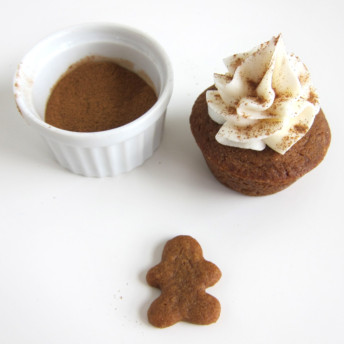 a white chocolate frosting swirl on top of a mini gingerbread cookie cup is sprinkled with cinnamon.